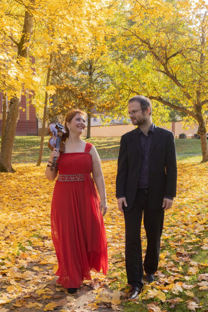 Das Duo Elegante läuft mit Geige über der Schulter umrahmt von Bäumen